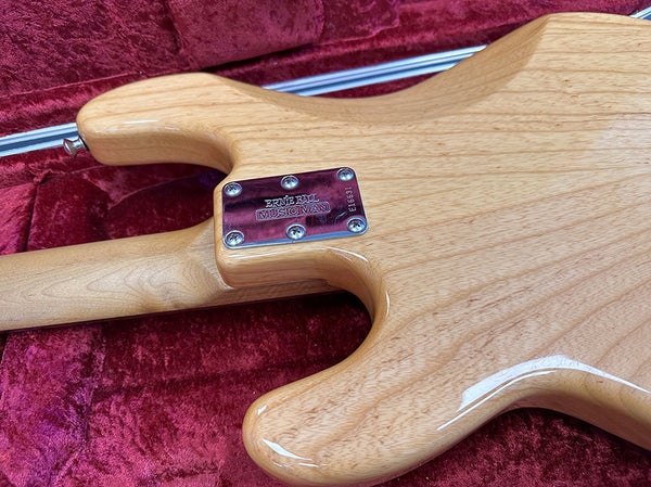 Close-up of Ernie Ball Music Man electric guitar rear neck plate on natural wood finish guitar body in red plush case