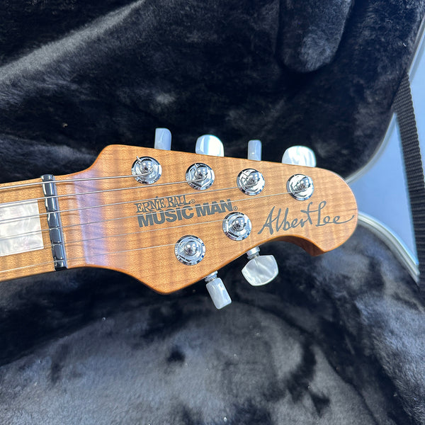 Close-up of Ernie Ball Music Man Albert Lee guitar headstock with tuning pegs and signature logo on natural wood finish in black plush guitar case