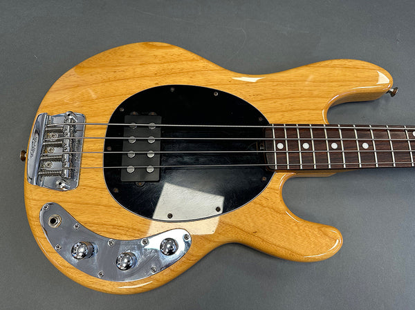 Natural finish electric bass guitar with black pickguard and chrome control knobs on gray background