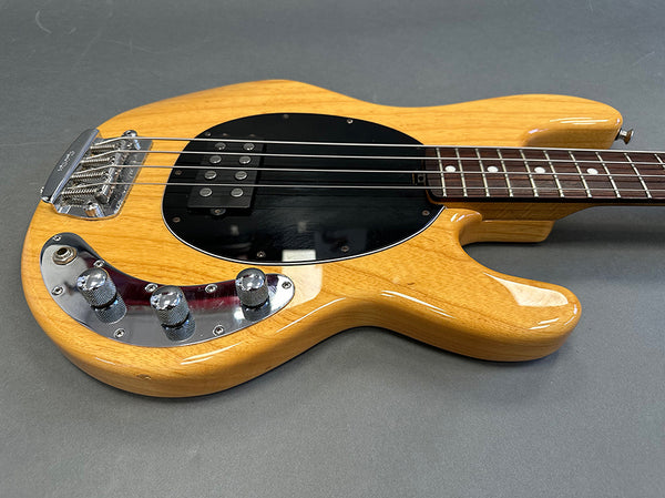 Natural finish electric bass guitar with black pickguard, chrome control knobs, and four strings on gray background