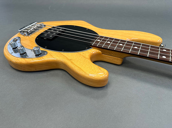 Natural wood finish electric bass guitar with black pickguard and chrome control knobs on gray background