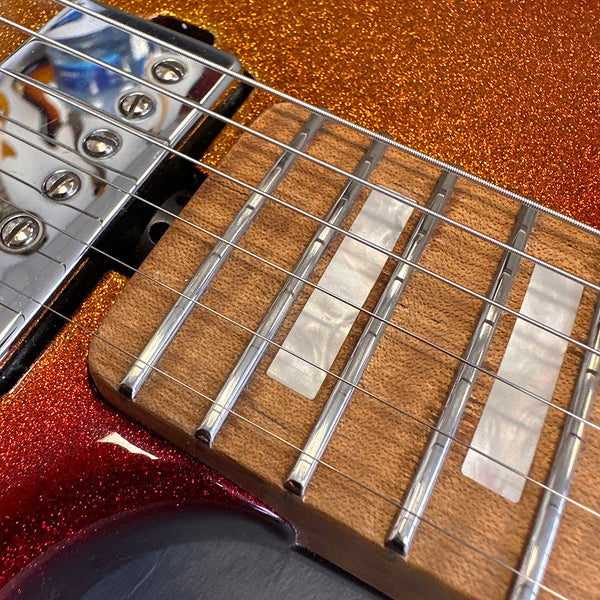 Close-up of electric guitar fretboard with pearl inlays, chrome frets, and orange sparkle finish body near pickup and strings.
