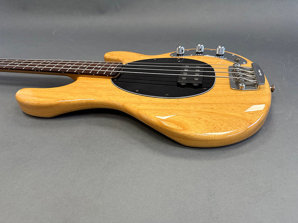 Natural wood finish electric bass guitar with black pickguard and chrome hardware on gray background