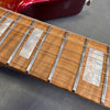 Close-up of guitar fretboard showing pearl block inlays, metal frets, and six guitar strings on light brown wood with part of red guitar body visible