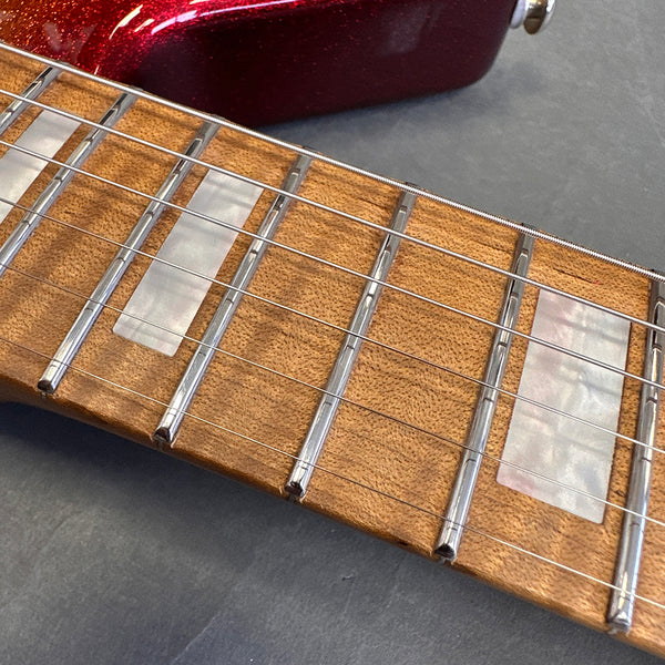 Close-up of guitar fretboard showing pearl block inlays, metal frets, and six guitar strings on light brown wood with part of red guitar body visible