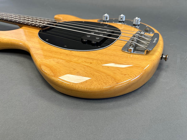 Close-up of natural wood finish electric guitar body with black pickguard and chrome bridge on gray background