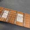Close-up of guitar neck showing rectangular mother of pearl inlays on a light brown wooden fretboard with metal frets and steel strings against a gray background