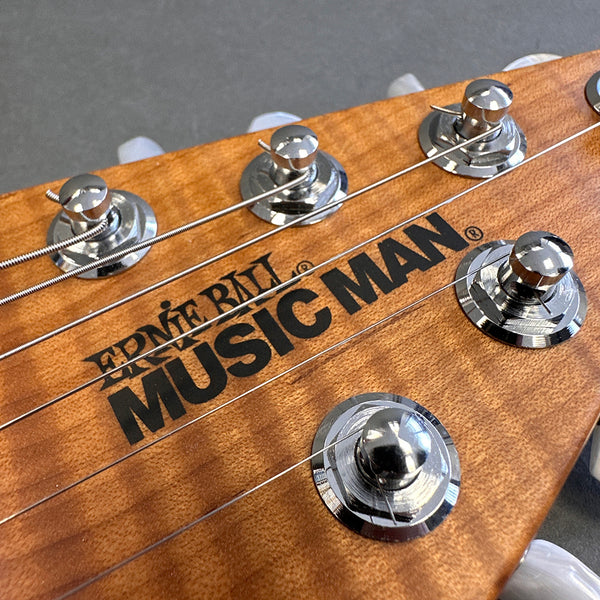 Ernie Ball Music Man guitar headstock close-up with tuning pegs and strings on natural wood finish