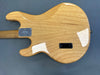 Back of natural finished electric guitar body showing wood grain and metal neck plate on gray background