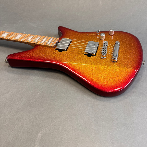 Electric guitar with metallic red to orange burst finish, maple fretboard, dual humbucker pickups, and chrome hardware on gray background
