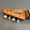 Close-up of amber figured wood guitar headstock with chrome tuning pegs and white tuning keys, labeled "Music Man Albert Lee"