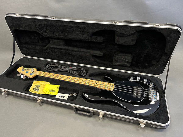 Black electric bass guitar with maple neck and fingerboard in open black hard case with cleaning cloth, cable, and accessory key inside Coffee House Guitars product listing