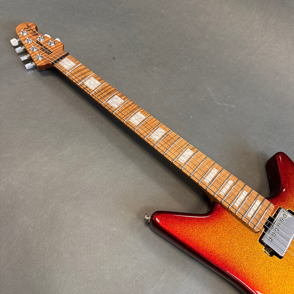 Electric guitar with flamed maple neck, rectangular pearl inlays, and metallic red to gold sunburst finish body on black background