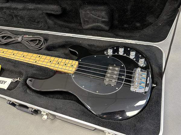 Black electric bass guitar with maple neck and chrome hardware in a black padded hard case with cable and accessory compartment