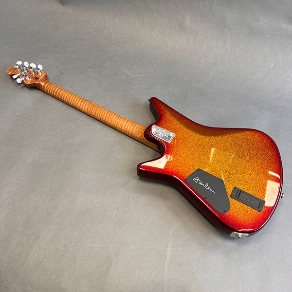 Back view of electric guitar with flamed maple neck and sunburst metallic finish body on gray surface