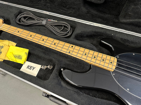 Black electric bass guitar with maple neck and fretboard in black padded hard case with guitar strap, polishing cloth, and tuning key accessories