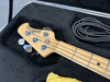 Close-up of a maple neck and headstock of a MusicMan Sterling electric bass guitar inside a black padded hard case with a coiled black guitar cable and yellow cleaning cloth.
