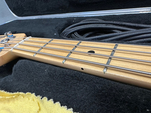 Close-up of a maple guitar neck with metal frets and four steel strings inside a black guitar case with a coiled black instrument cable and a yellow cleaning cloth.