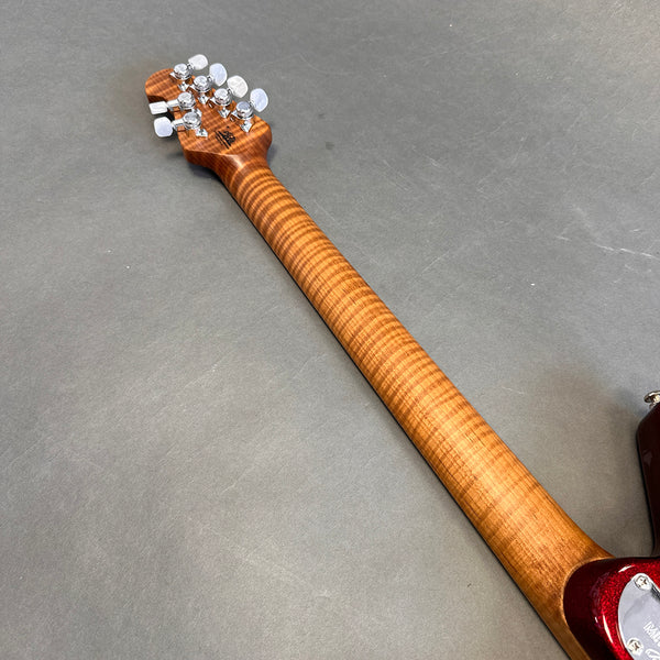 Back of electric guitar neck showing flamed maple wood grain and chrome tuning pegs on gray background