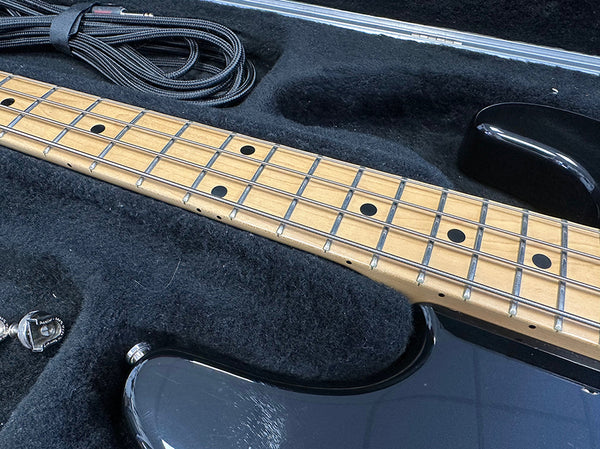 Close-up of maple fretboard and black body of electric bass guitar resting in black plush guitar case with black guitar strap inside