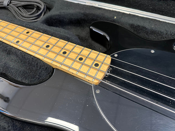 Close-up of maple fretboard and black body of electric bass guitar in a padded guitar case with cable.