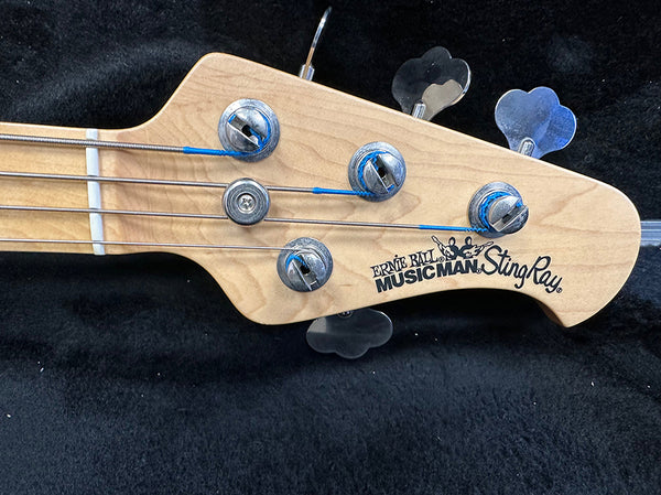 Close-up of Ernie Ball Music Man Sting Ray bass guitar headstock with tuning pegs and strings on black background