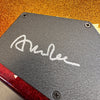 Close-up of guitar backplate with signature on textured black cover plate and metallic red and orange guitar body finish from Coffee House Guitars