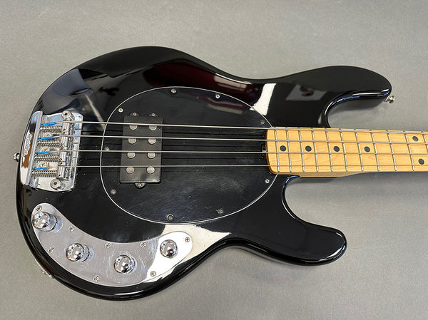 Black electric bass guitar with maple fretboard, chrome bridge, and control knobs on grey background