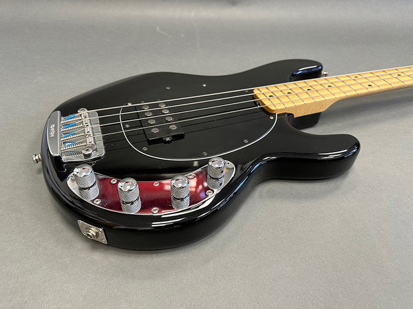 Black electric bass guitar with maple neck and chrome control knobs on gray background, close-up angle