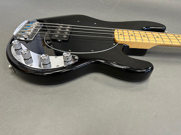 Black electric bass guitar with maple neck, chrome control knobs, and black pickguard on gray background