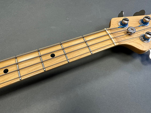Close-up of maple bass guitar neck and headstock with chrome tuning pegs and metal strings on gray background