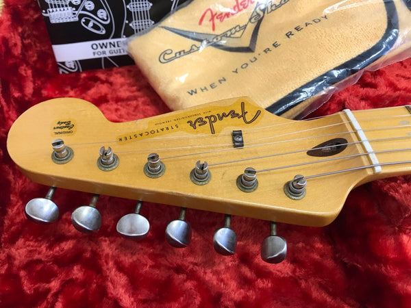 Close-up of vintage Fender Stratocaster guitar headstock with six tuning pegs, original Custom Body decal, and Fender Custom Shop polishing cloth on red plush background