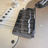 Close-up of Fender electric guitar chrome bridge, white pickguard, volume control knob, and single-coil pickup with guitar strings attached