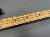 Maple fretboard close-up with black dot inlays and metal frets on electric bass guitar neck against gray background.
