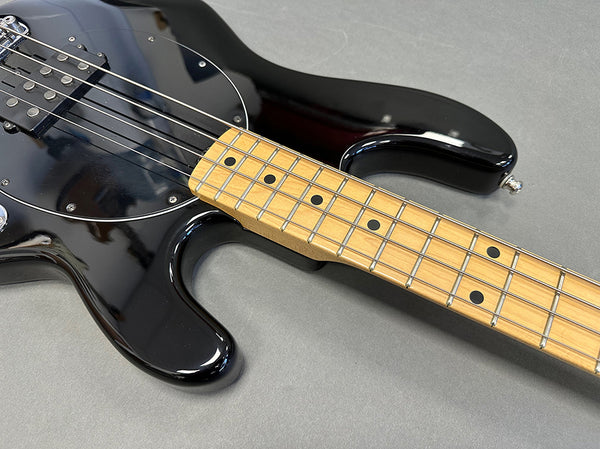 Close-up of black electric bass guitar body and maple fretboard with black dot inlays on gray surface at Coffee House Guitars