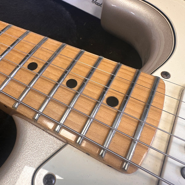 Close-up image of maple guitar neck and fretboard with black dot inlays on an electric guitar body.