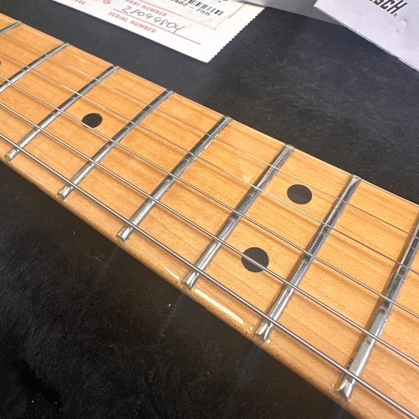 Close-up of maple guitar fretboard with metal frets and black dot inlays on a six-string electric guitar neck in a black case