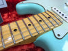 Close-up of maple neck and frets on seafoam green electric guitar with white pickups on red plush background