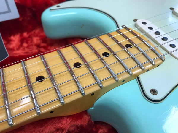 Close-up of maple neck and frets on seafoam green electric guitar with white pickups on red plush background