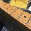 Close-up of maple guitar neck and fretboard with metal frets and black dot inlays, guitar strings installed, with yellow cleaning cloth in the background on a black surface.