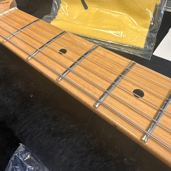 Close-up of maple guitar neck and fretboard with metal frets and black dot inlays, guitar strings installed, with yellow cleaning cloth in the background on a black surface.
