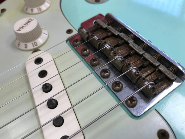 Close-up of electric guitar bridge, rusty saddles, strings, volume knob, and single-coil pickup on seafoam green body