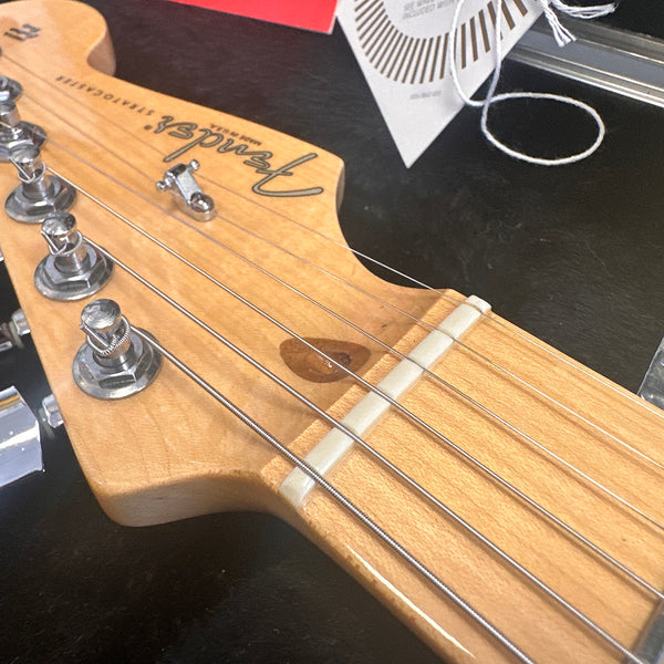 Close-up of Fender Stratocaster electric guitar headstock with tuning pegs and strings on a black surface