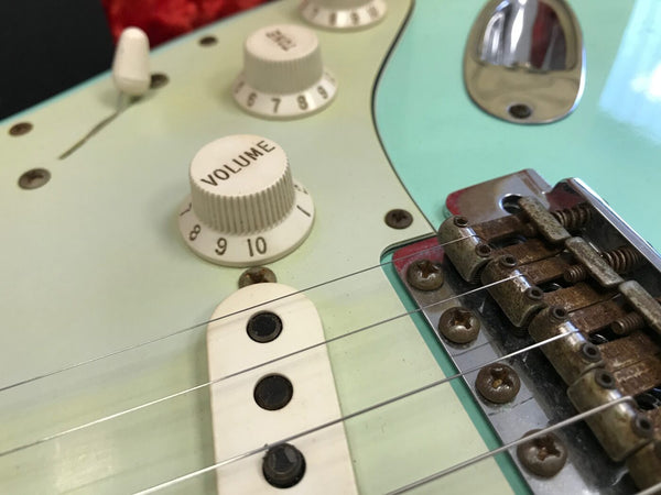 Close-up of volume knob, pickup, and bridge on a light blue electric guitar with vintage-style components and rusted bridge saddles at Coffee House Guitars.