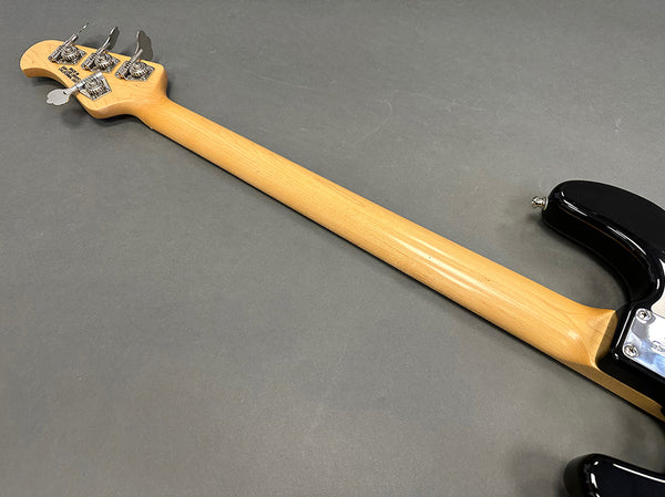 Maple neck and silver tuning pegs on black electric bass guitar shown from back on gray background