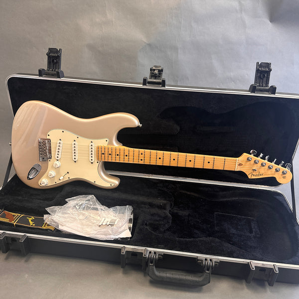 Fender Stratocaster electric guitar in metallic champagne finish with maple neck and fretboard, in black plush-lined hard case with Fender strap and plastic packaging.