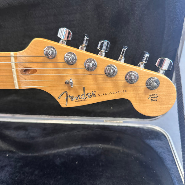 Close-up of Fender Stratocaster guitar headstock with chrome tuning pegs and natural wood finish inside a hard guitar case