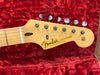 Close-up of Fender Stratocaster guitar headstock with tuning pegs on red plush guitar case interior