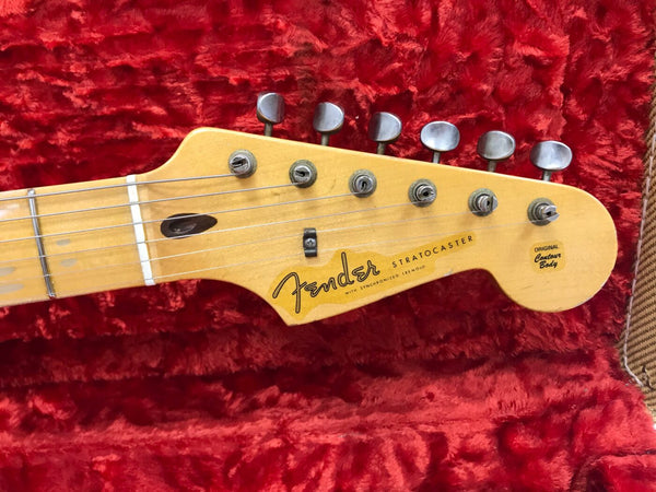 Close-up of Fender Stratocaster guitar headstock with tuning pegs on red plush guitar case interior