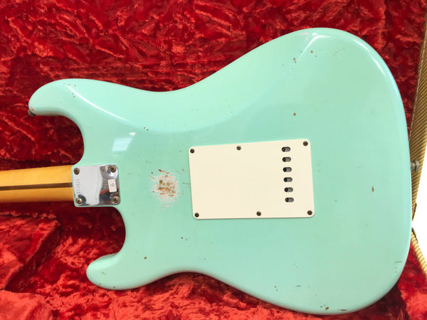 Back view of light blue electric guitar with white plastic cover plate and visible wear spots, lying on red textured fabric background